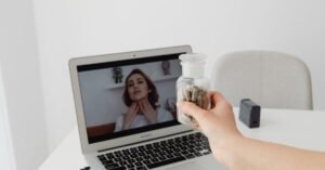 Une personne tient un pot de gélules de shilajit, étiquetées shilajit pur, shilajit en bocal, shilajit resine, à côté d'un ordinateur portable avec une femme à l'écran.