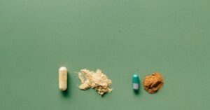 Une capsule jaune, shilajit, shilajit pur, un petit tas de poudre beige, shilajit en bocal, une capsule verte et blanche, shilajit resine, et un petit tas de poudre brune sont disposés en ligne sur une surface verte.